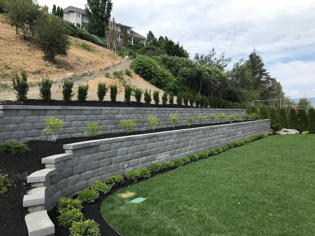 2 retaining walls with neatly stacked stone a green lawn and multiple small bushes